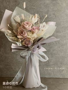 a bouquet of flowers in a white vase with ribbon tied around the bottom and side