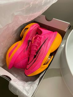 a pair of pink and yellow nike shoes in a box next to a white sink