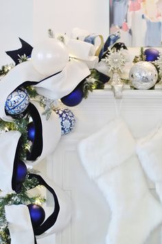 white and blue christmas decorations are hanging on the mantel