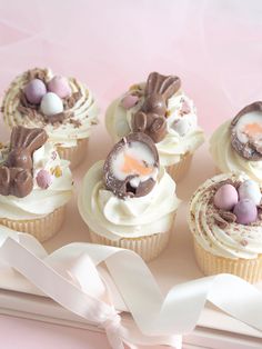 several cupcakes with white frosting and chocolate bunny ears on top are sitting on a pink surface