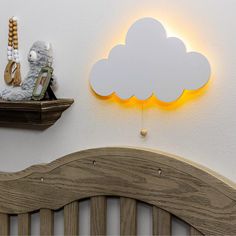 a teddy bear sitting on top of a bed next to a cloud shaped wall light