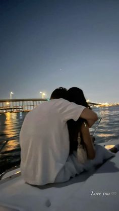 a man and woman sitting on the back of a boat looking out over water at night