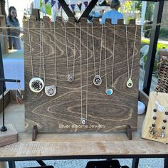 a wooden sign with several different necklaces hanging from it's sides on a table