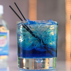 a blue liquid in a glass with two black straws sticking out of the top