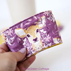 a hand holding a purple and white fabric with a deer on it