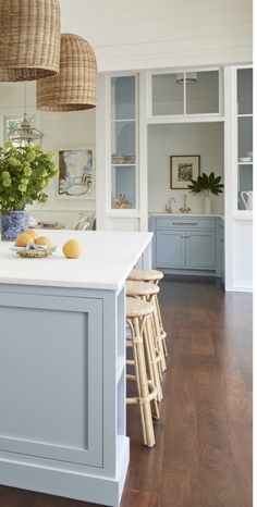 a kitchen with blue cabinets and white counter tops, wooden stools and baskets hanging from the ceiling