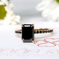 a black diamond ring sitting on top of a white paper with flowers in the background