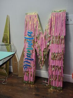 the letters are made out of pink and gold fringed material with blue lettering on them