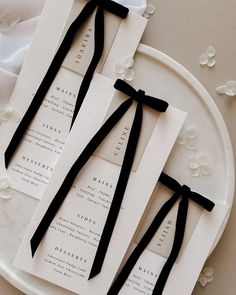 two black ties are tied to the back of some white wedding programs on a plate