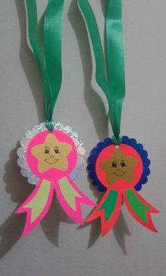 two paper flowers with faces on them are hanging from green ribbon and another one has a pink flower in the middle