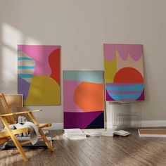 three paintings hang on the wall next to a chair in a room with hard wood floors