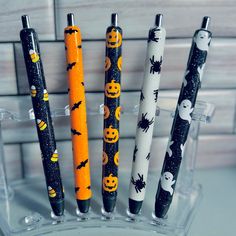 four halloween themed pens sitting on top of a glass holder with bats and pumpkins