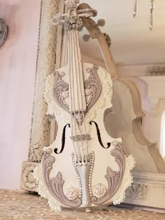 a white violin sitting on top of a table in front of a mirror and chandelier