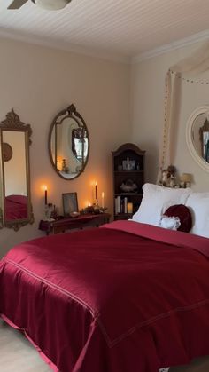 a bed with red sheets and pillows in a bedroom next to two mirrors on the wall