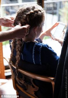 a woman sitting in a chair while getting her hair braided by someone with a cell phone