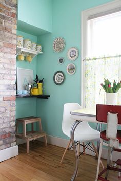 a dining room with blue walls and wood floors, white chairs and a brick fireplace