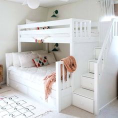 a white bunk bed sitting next to a stair case in a room with carpeted flooring