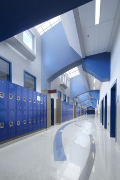 an empty school hallway with blue lockers and white flooring on both sides of the hall