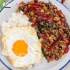 a white plate topped with rice, meat and an egg next to a fried egg