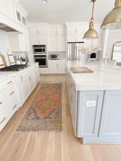 a large kitchen with white cabinets and wooden flooring, along with a rug on the floor