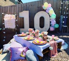 a table set up for an outdoor birthday party with balloons and flowers on the table