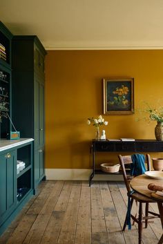 a table and chairs in a room with yellow walls, wooden floors and green cabinets