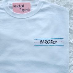 a white t - shirt with stitched words on the front and back, sitting on a fluffy surface