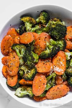 a bowl filled with broccoli and carrots on top of a white table