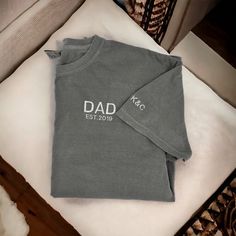 "These embroidered Dad T-shirts make a great Father's Day gift! Customized with the year they became a dad and the kids initials on the sleeve! **If you would like this shirt customized beyond adding the est. year and initials on the sleeve, please email us first to make sure that the changes are possible. There will be a $10 charge for extra customization outside of est. year and initials. We will then let you know to pick the \"extra customization\" option in the color selection in the size you need. When doing this please put the color shirt you would like from the available options in the personalization box along with your other customizations.**  ORDERING & SHIPPING *Your item will be shipped within 5-7 business days. *Please allow 2-5 business days to receive your item, more time ma Dad Shirts Father's Day, Personalized Cotton T-shirt For Father's Day, Personalized Cotton T-shirt With Letter Print, Personalized Cotton T-shirt With Short Sleeves, Personalized Cotton Short Sleeve T-shirt, Personalized Gift Cotton T-shirt With Short Sleeves, Father's Day Personalized Cotton T-shirt, Custom Text Cotton Tops For Personalized Gift, Personalized Cotton T-shirt With Custom Text