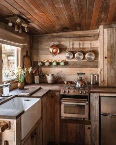 a rustic kitchen with wooden walls and flooring, pots on the wall, an oven, sink, and dishwasher