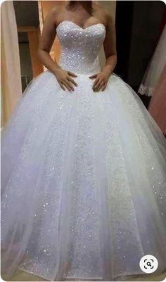 a woman wearing a white wedding dress standing in front of a mirror with her hands on her hips