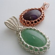 two wire wrapped pendants with green and purple stones in them on a white surface