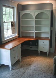 an empty room with a desk and bookcase next to a window in the corner