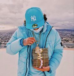 a man in a blue jacket holding stacks of money wearing a new york yankees hat