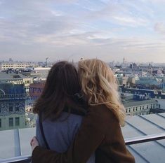 two people standing on top of a building looking at the city