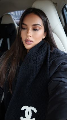 a woman sitting in the back seat of a car wearing a black sweater and scarf