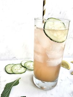 a cucumber drink in a tall glass with a straw and sliced cucumbers around it