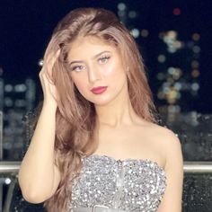 a beautiful young woman in a silver dress posing for the camera with her hand on her head