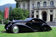 an old black car parked in front of a large building