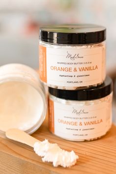 Stack of two body butter containers labeled "Orange & Vanilla" made by Mad Sass Soap Co. Stick with body butter in the foreground and open jar in the background. Handmade Body Butter, Organic Shea Butter