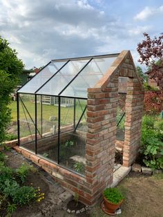 a small brick building with a glass roof in the middle of a garden filled with plants