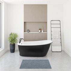 a bath tub sitting next to a window in a white and black bathroom with a rug on the floor