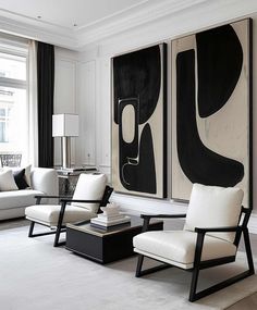 a living room filled with white furniture and black paintings on the wall above two couches