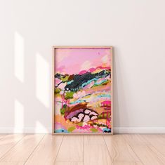 an abstract painting in a wooden frame on the floor next to a white painted wall