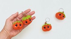 a hand holding three small crocheted pumpkins with eyes and noses on them