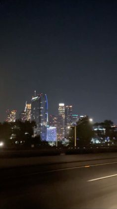 the city skyline is lit up at night with skyscrapers in the distance and cars driving on the road