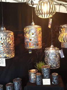 many lamps are hanging from the ceiling and decorated with intricate designs on display at an outdoor market