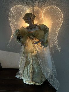 a lighted angel figurine sitting on top of a wooden table next to a wall