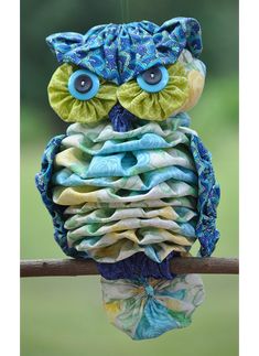 a stuffed owl sitting on top of a wooden branch with blue eyes and green leaves