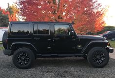 a black jeep is parked in front of some trees with orange and red leaves on it